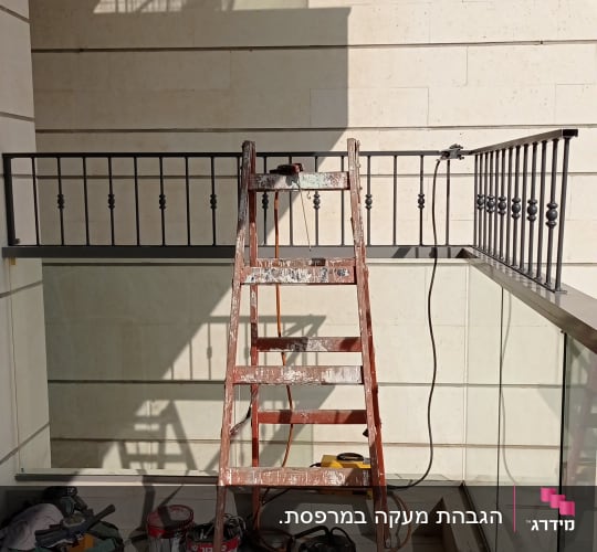 סולם עץ מול מעקה מתכת עם כלים על הרצפה